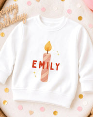 A white sweatshirt with a personalized name printed on it, along with a candle design.