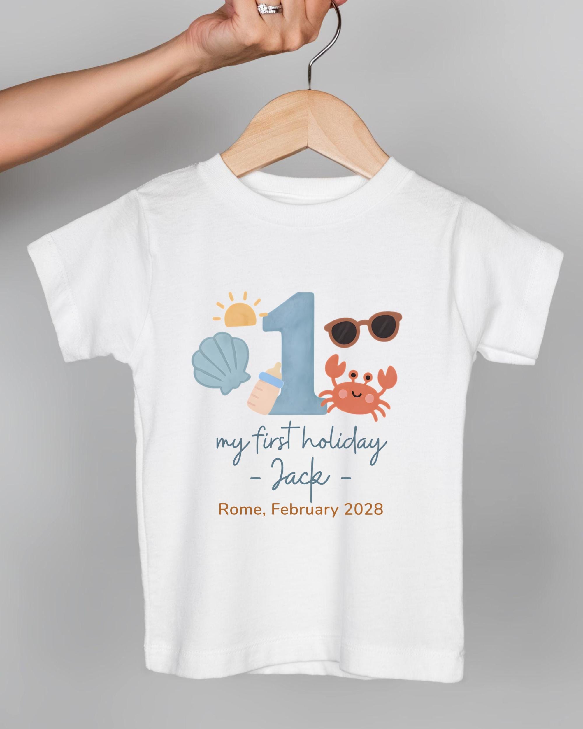 A white t-shirt with a graphic design featuring a number 1, sunglasses, a crab, and text that says "my first holiday - Jack - Rome, February 2028".