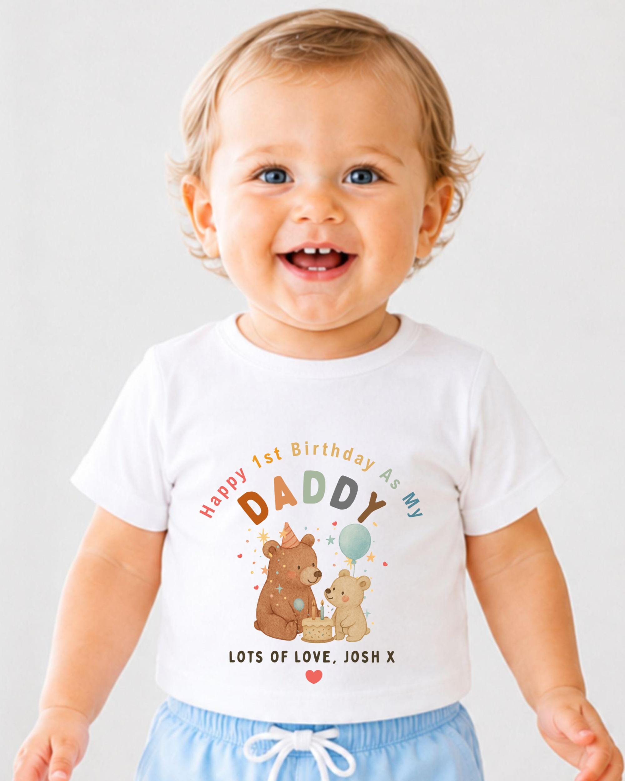 A smiling baby boy wearing a white t-shirt with a birthday message and illustrations of bears.