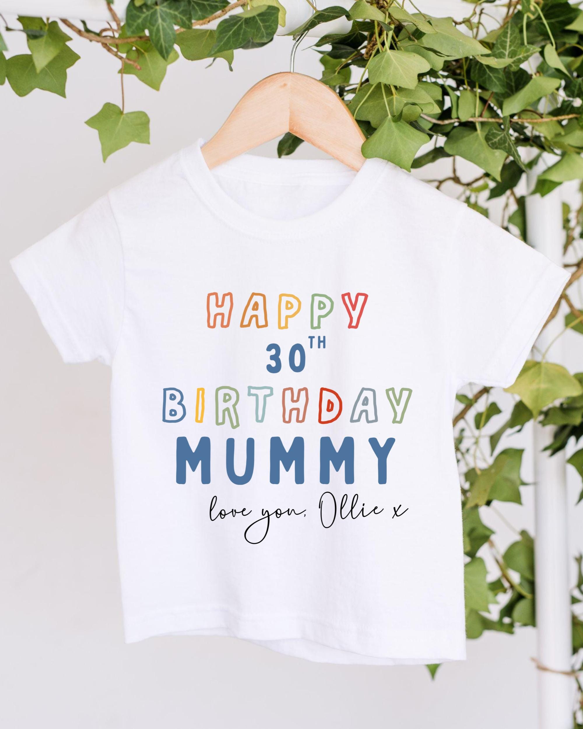 A white t-shirt with a colorful text message that reads "Happy 30th Birthday Mummy love you: Ollie X" printed on it.