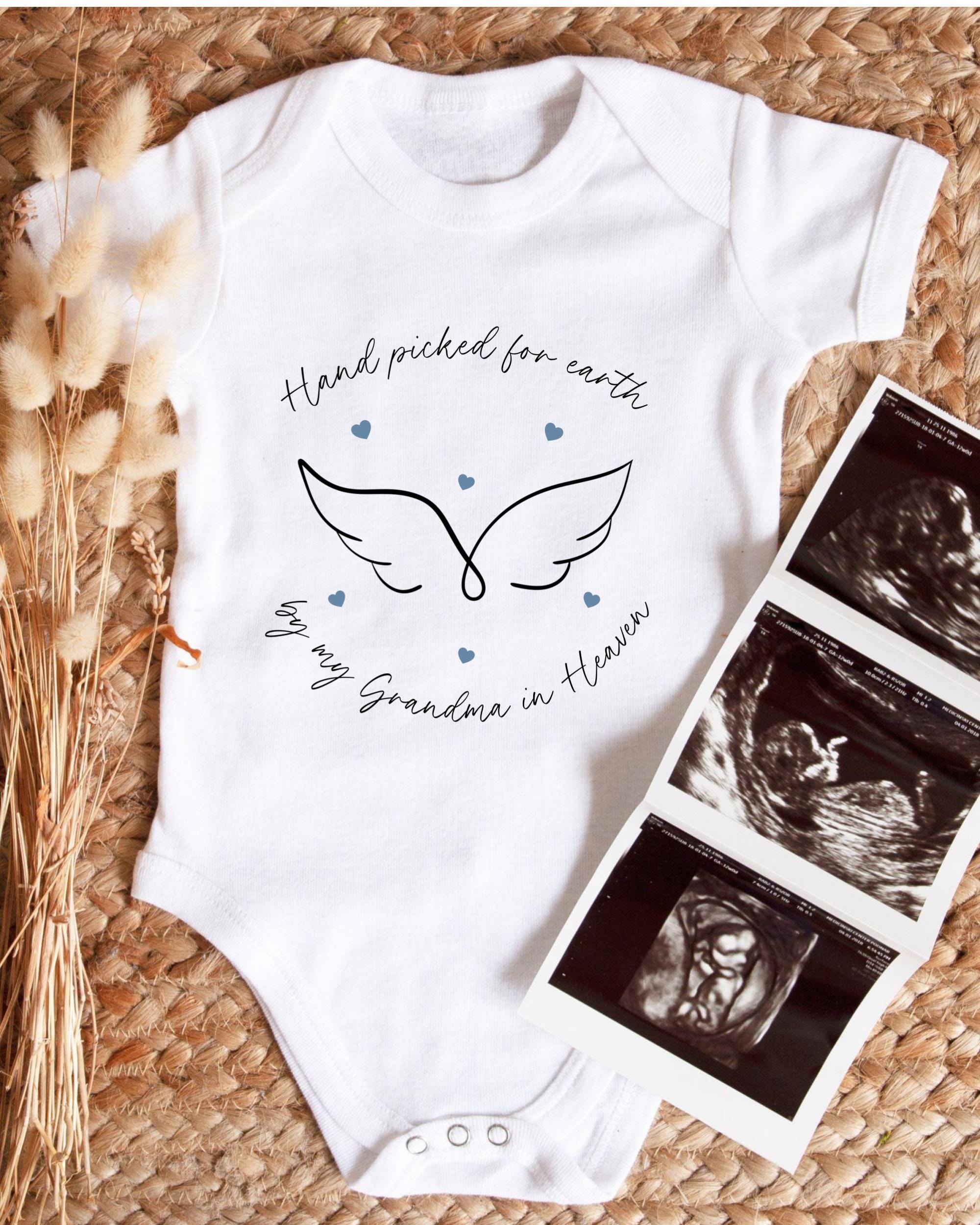 A white baby onesie with a graphic design and text, placed next to a set of black and white medical images, likely from an ultrasound.