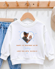 A white sweatshirt with a heart-shaped photo of a man holding a baby, along with the text "Happy 1st Birthday as my Daddy, Love You Lots, Olivia X" printed on it.