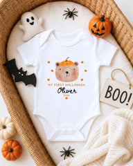 A white onesie with a bear and pumpkin design, surrounded by Halloween decorations such as a ghost, a pumpkin, a bat, and a sign that says "BOO!".