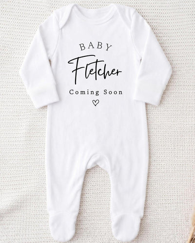 Personalisable white Baby Grow with black 'Baby Fletcher Coming Soon' serif and script lettering and a small outlined heart.