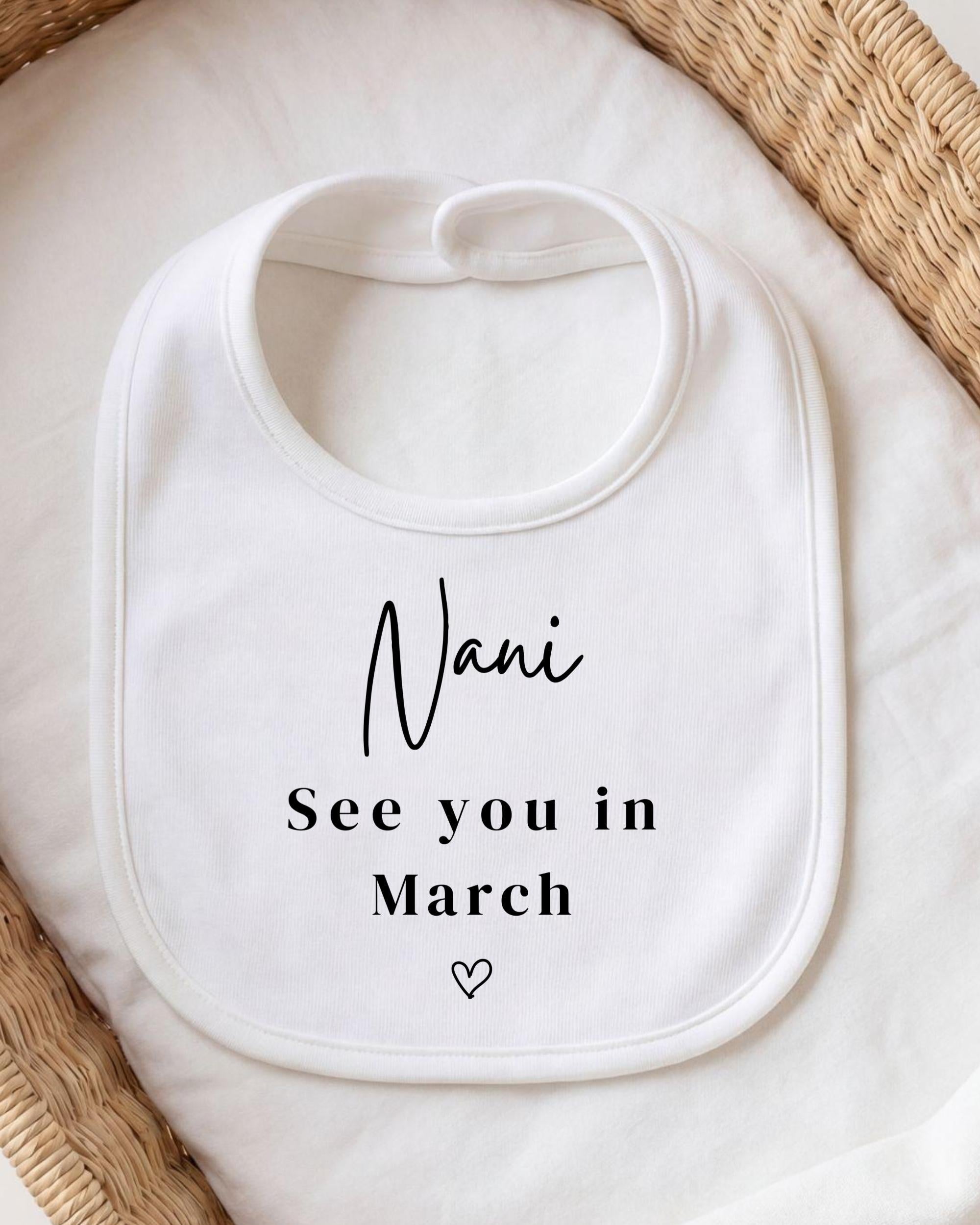 A white bib with the text "Nani See you in March" printed on it, placed on a white cloth.