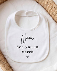 A white bib with the text "Nani See you in March" printed on it, placed on a white cloth.