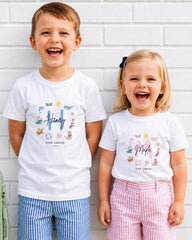 Two children, a boy and a girl, are standing next to each other and smiling. They are wearing matching white t-shirts with colorful designs and text.