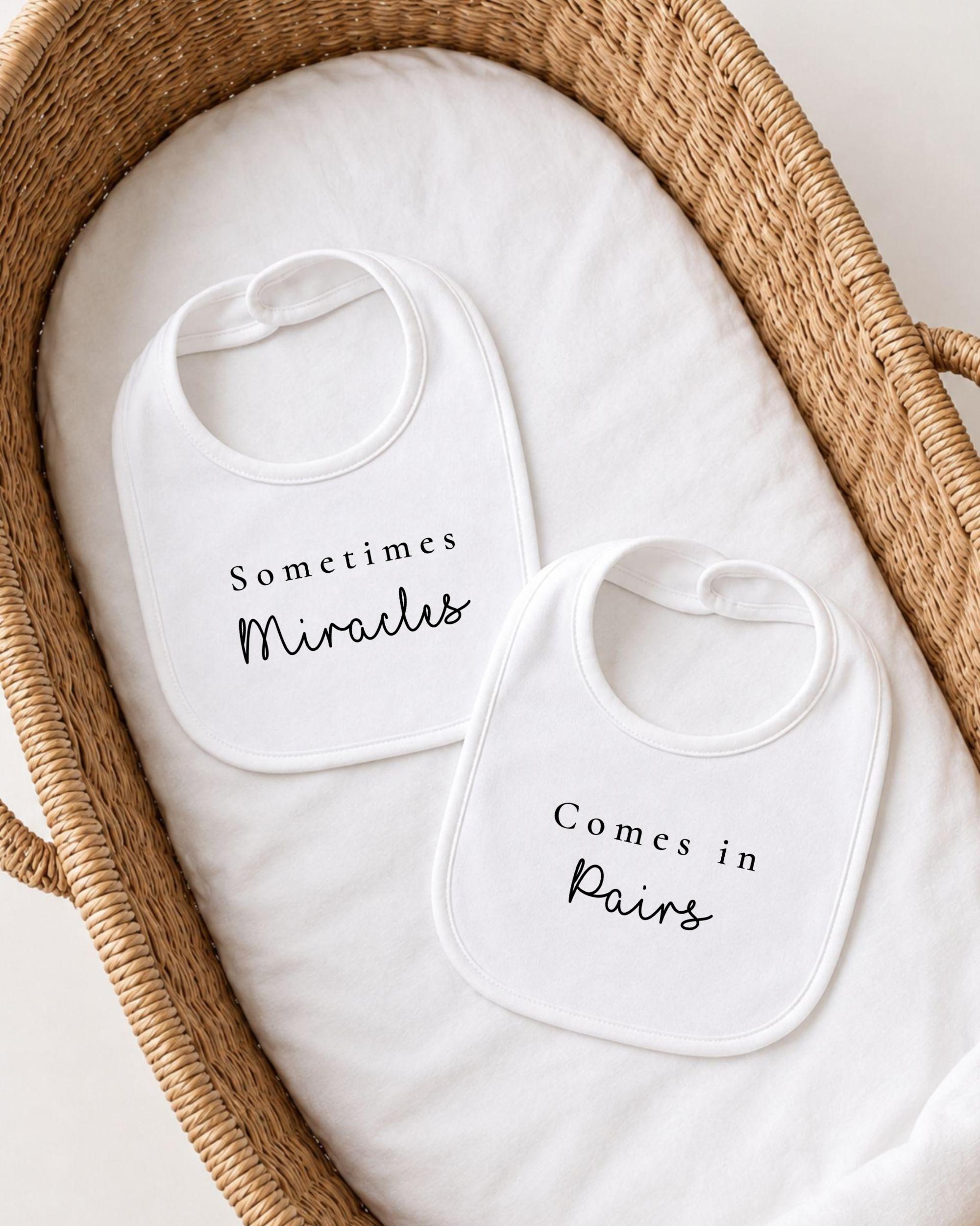 two white bibs with black text, placed in a woven basket.