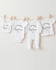 A row of white baby clothes with the text "I love auntie Sophie" printed on them, hanging on a clothesline.