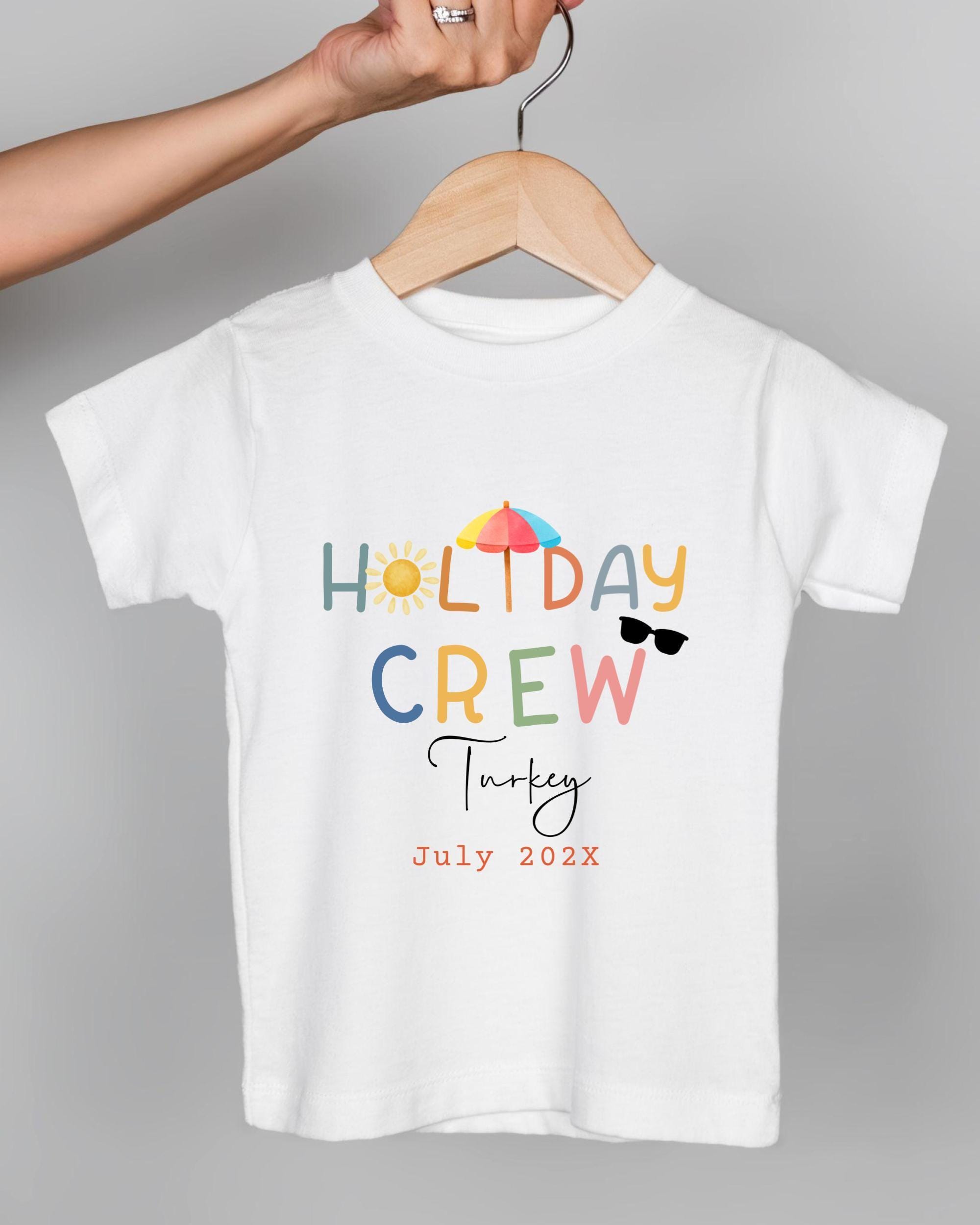 A white t-shirt with colorful text and graphics, including the words "HOLIDAY CREW" and "July 2023", suggesting a summer-themed design.