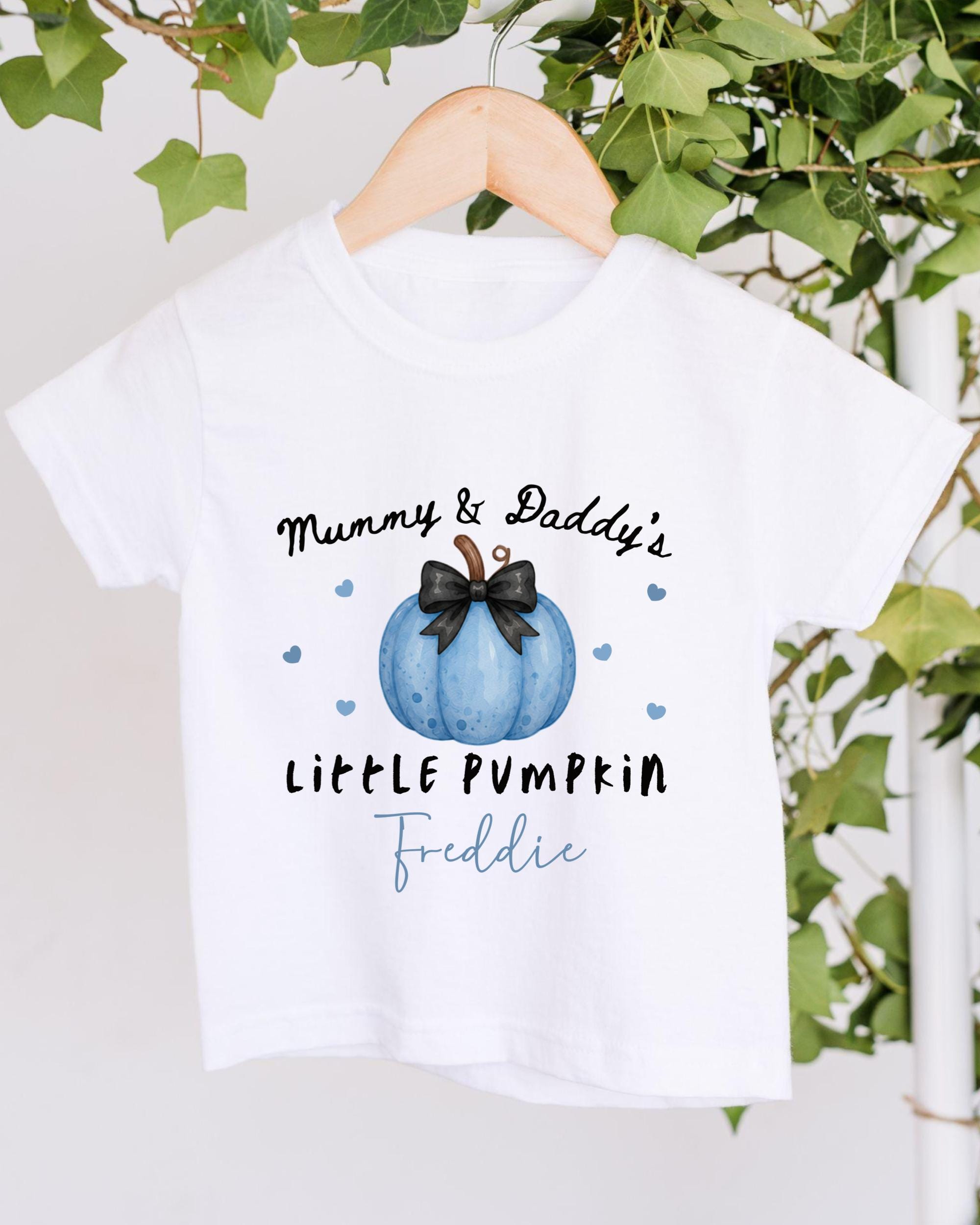 A white t-shirt with a graphic design featuring a blue pumpkin and the text "Mummy & Daddy's LITTLE PUMPKIN Freddie" printed on it.