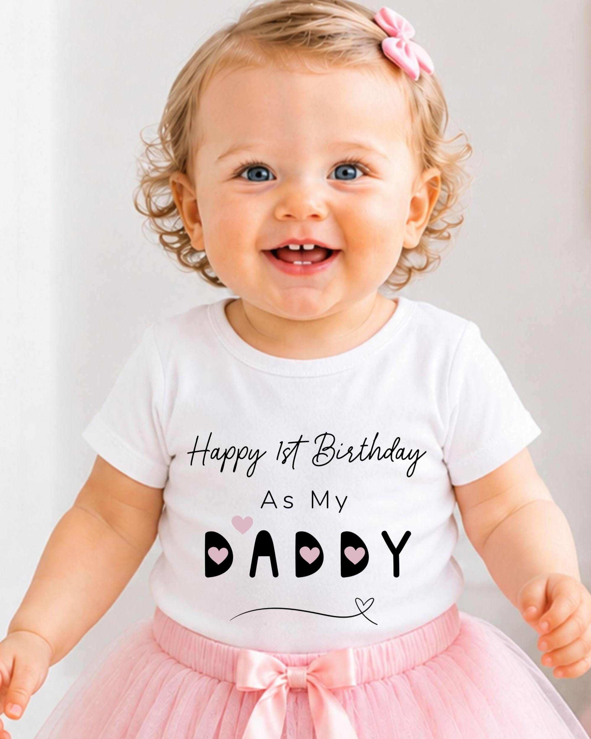 A smiling baby girl wearing a white t-shirt with text and a pink bow, standing in front of a white background.