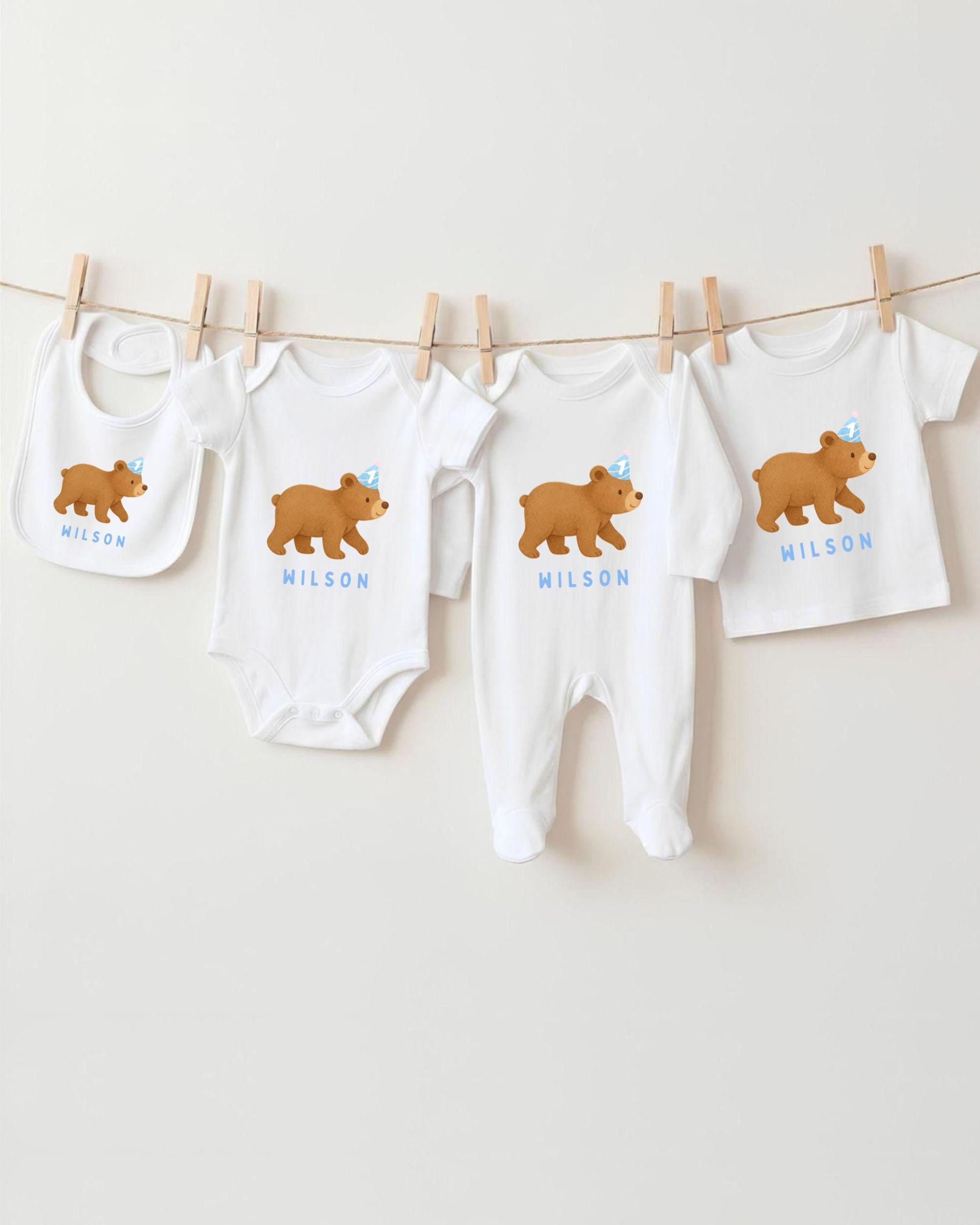 A collection of baby clothes, including onesies and bibs, featuring a brown bear design.