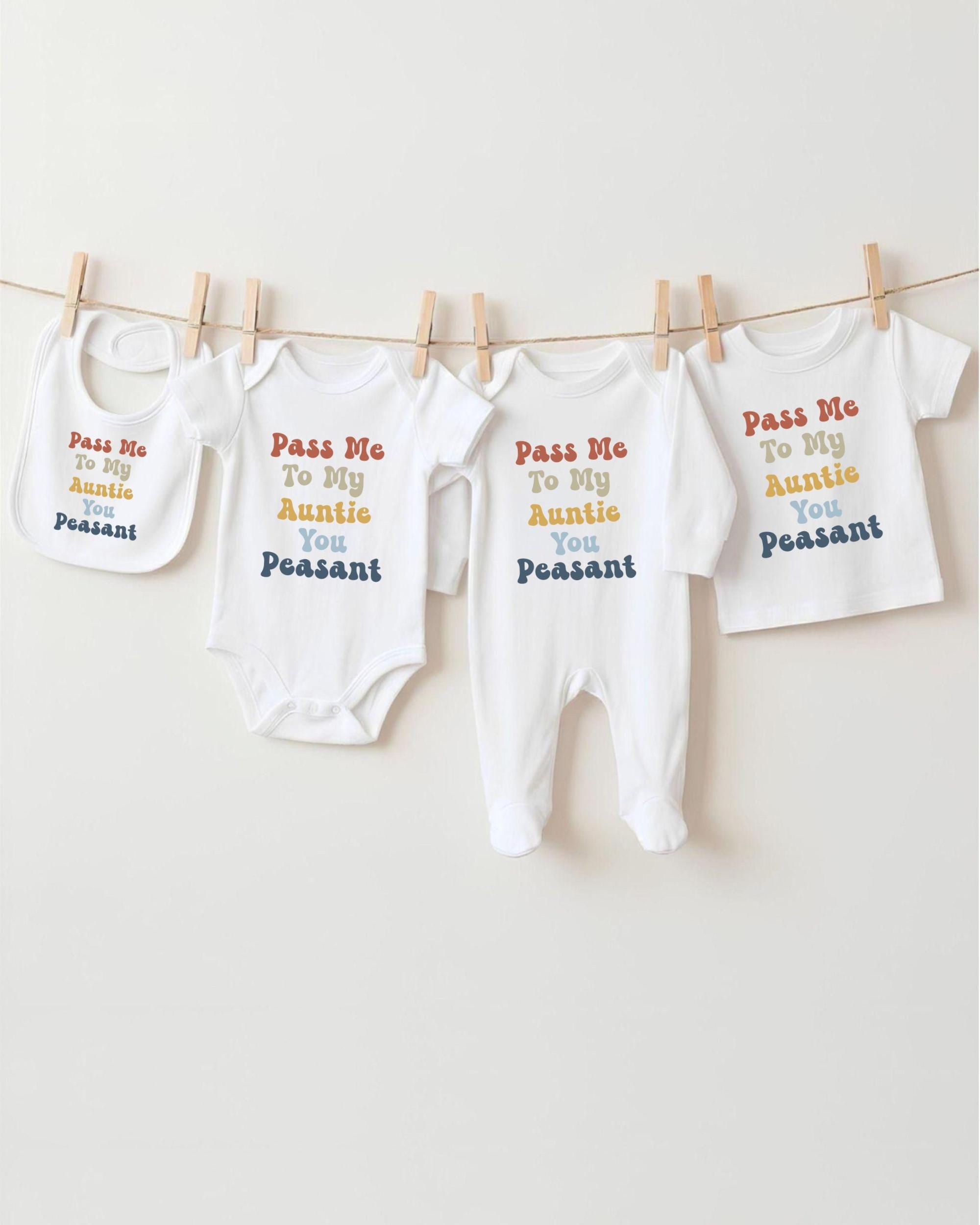 A row of four white baby clothes hanging on a clothesline, each with a different message printed on it.
