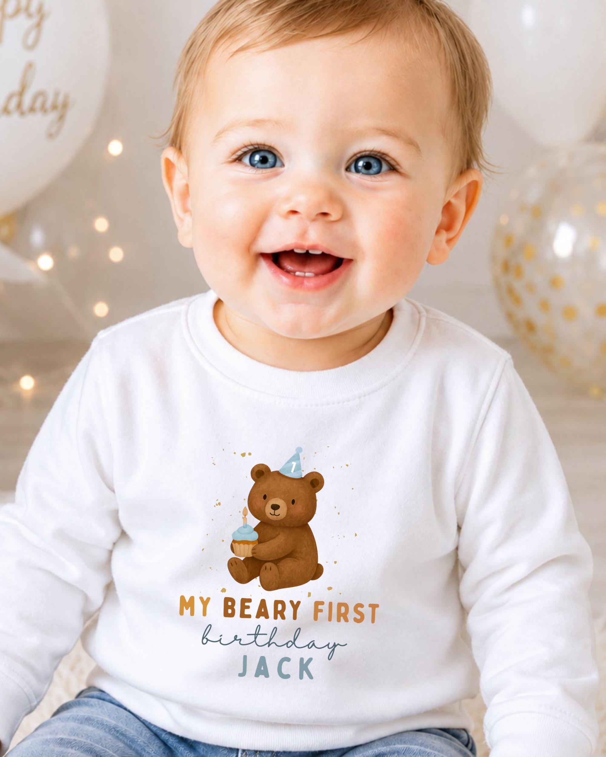 A smiling baby boy wearing a white shirt with a teddy bear and text that says "My Beary First birthday Jack".