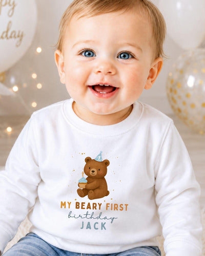 A smiling baby boy wearing a white shirt with a teddy bear and text that says "My Beary First birthday Jack".