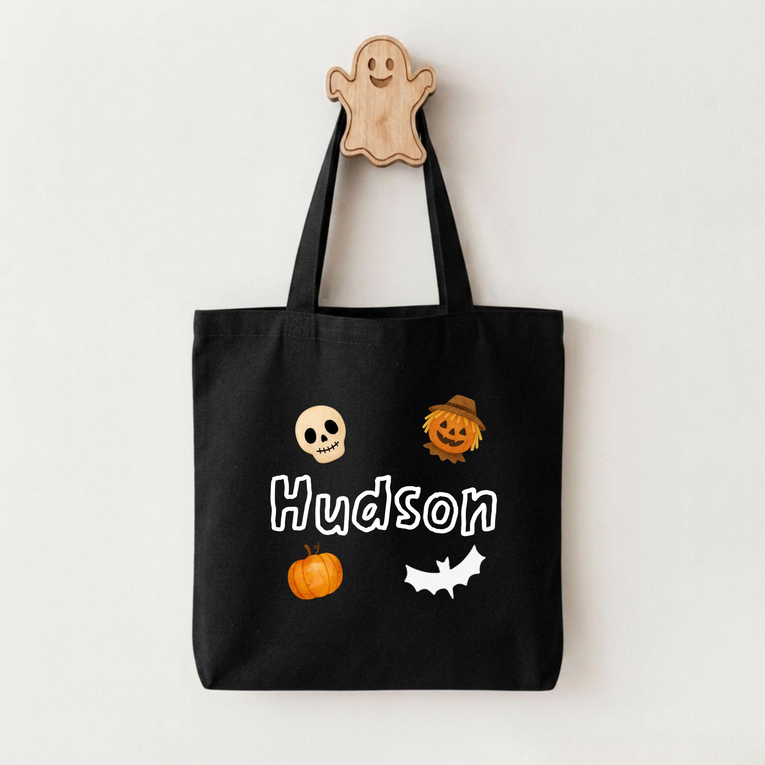 A black tote bag with Halloween-themed stickers and a wooden ghost hanger.