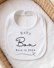 A white baby bib with the text "Baby Box" printed on it, placed on a white cloth.