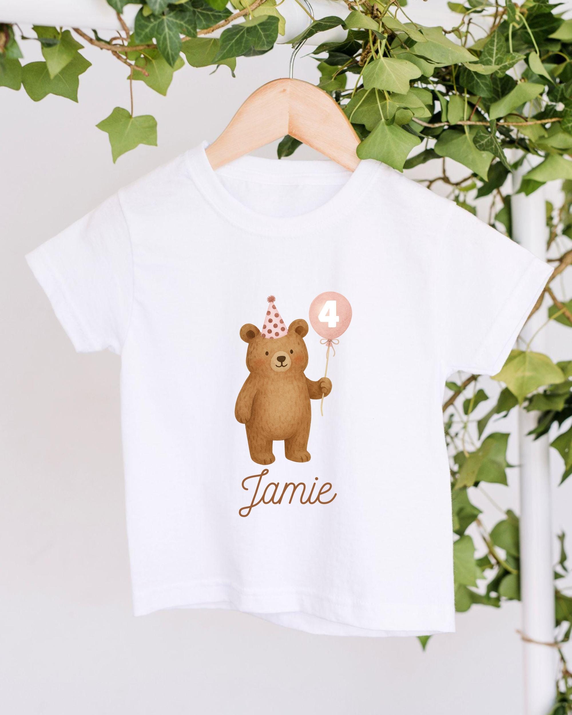 A white t-shirt with a cartoon image of a bear wearing a party hat and holding a balloon, along with the name "Jamey" printed on it.