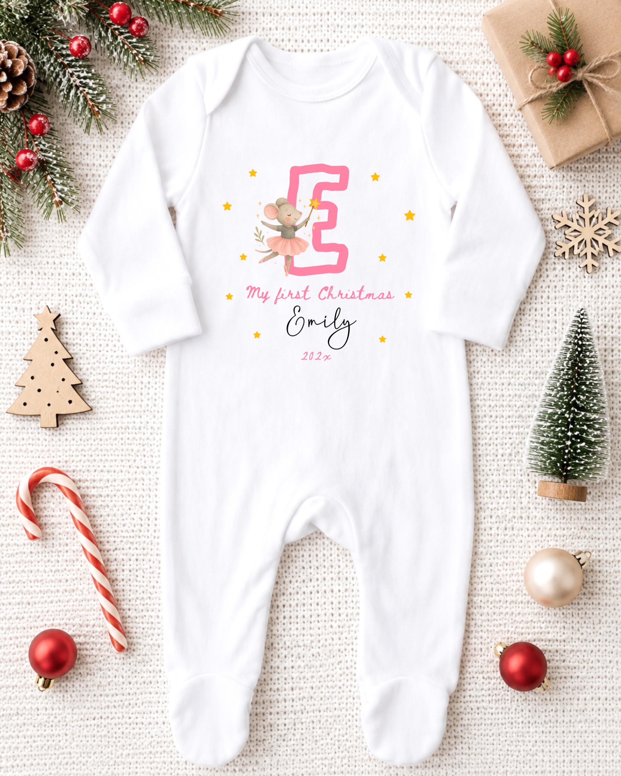 A white onesie with a pink letter "E" and a small mouse, surrounded by Christmas decorations and gifts.