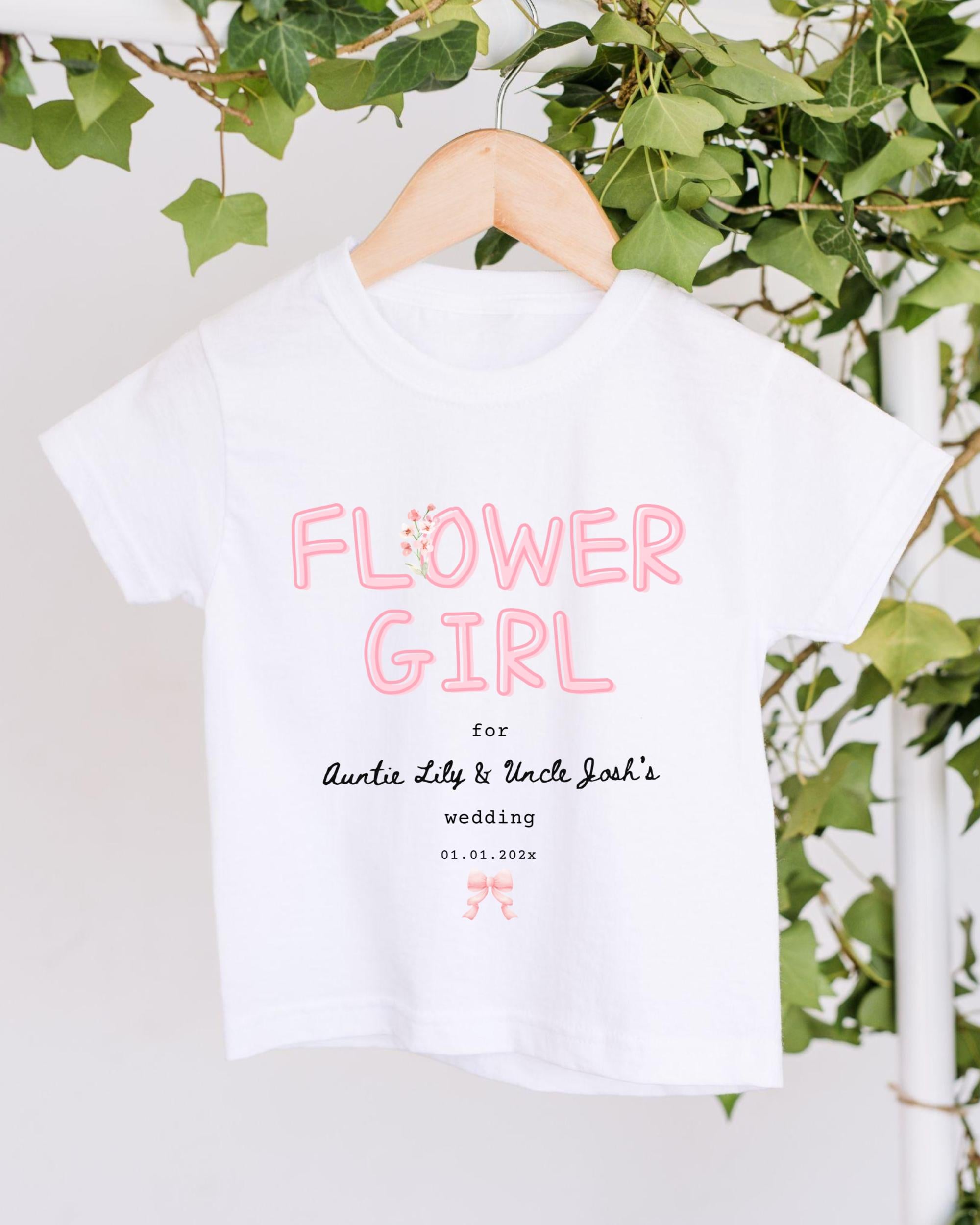 A white t-shirt with pink text and a date printed on it, hanging on a wooden hanger.