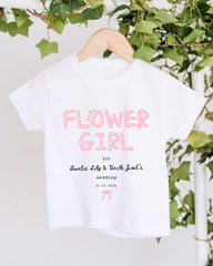 A white t-shirt with pink text and a date printed on it, hanging on a wooden hanger.