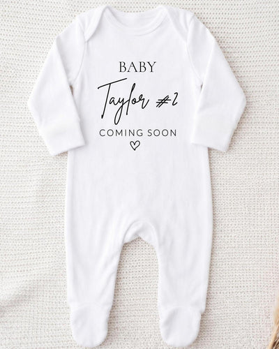 A white bodysuit with the text "BABY Taylor #2 COMING SOON" printed on it.