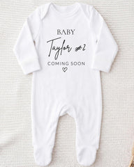 A white onesie with the text "BABY Taylor #2 COMING SOON" printed on it.
