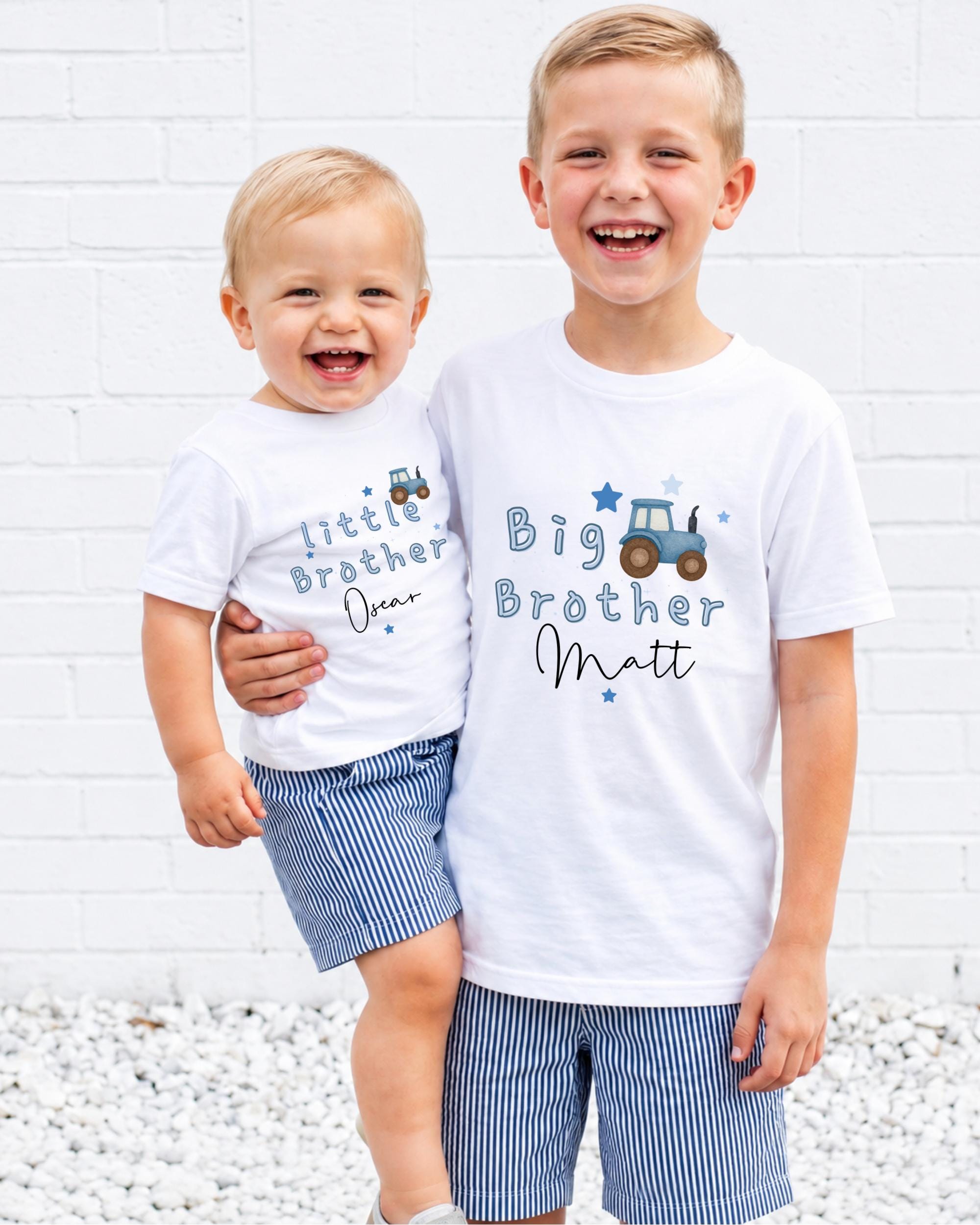 Two young boys wearing matching white t-shirts with blue designs and text, smiling and posing together.