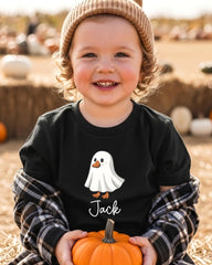 A young child wearing a black t-shirt with a ghost and the name "Jack" printed on it, holding a small orange pumpkin.