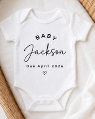 A white baby onesie with the text "BABY JACKSON Due April 2026" printed on it.
