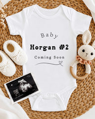 Baby clothing, baby shoes, a crocheted rabbit toy, and an ultrasound image are arranged on a woven mat.