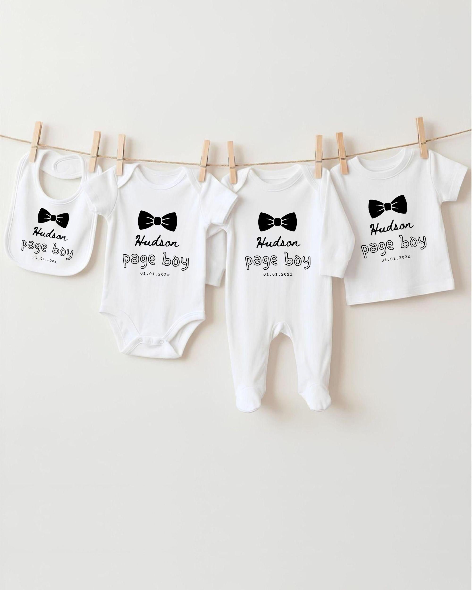 A row of four white baby clothes with black text and bow ties, hanging on a clothesline.