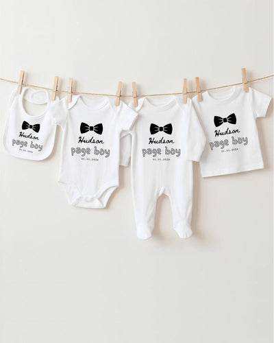 A row of four white baby clothes with black text and bow ties, hanging on a clothesline.