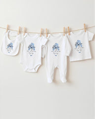 A row of white baby clothes, including onesies and bibs, hanging on a clothesline.