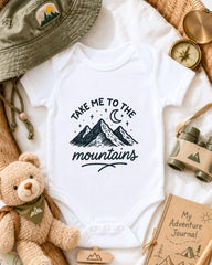 a baby onesie with a mountain and starry night sky design, surrounded by various outdoor-themed items such as a hat, compass, binoculars, and a teddy bear.