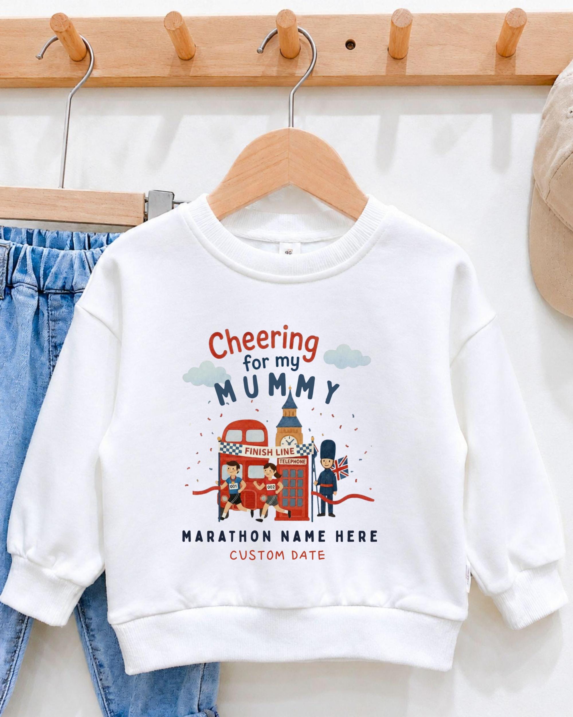 A white sweatshirt with a graphic design featuring a red double-decker bus, a person in a British hat, and the text "Cheering for my Mummy" and "Marathon Name Here Custom Date".