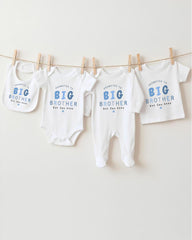 A row of baby clothes, including bibs and onesies, hanging on a clothesline.