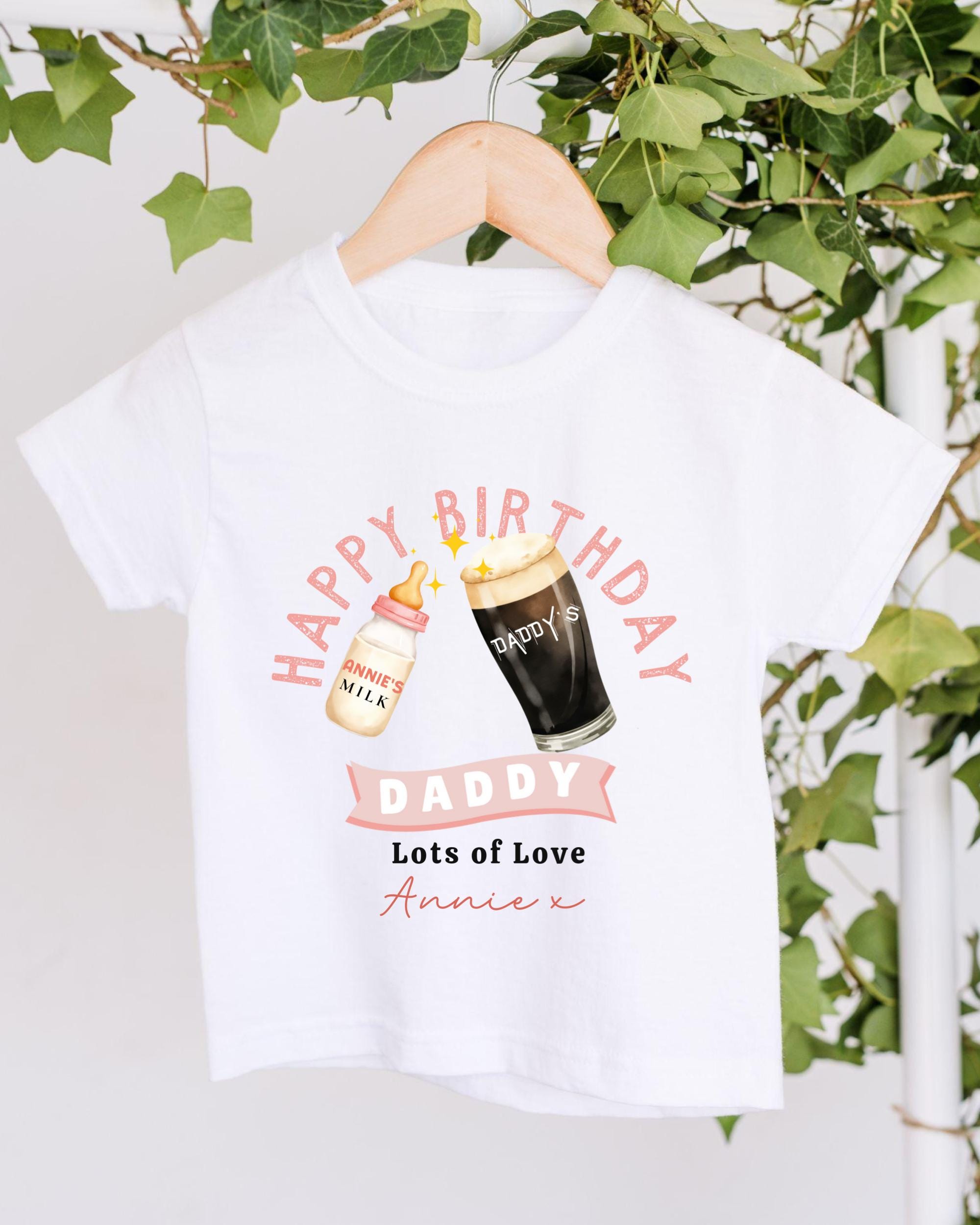 A white t-shirt with a graphic design featuring a bottle of milk and a glass of beer, along with the text "Happy Birthday Daddy Lots of Love Anniex".