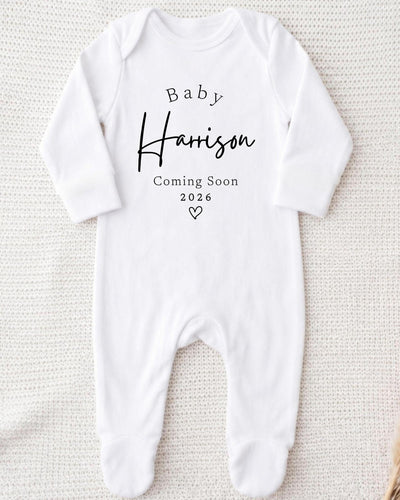 A white bodysuit with the text "Baby Harrison Coming Soon 2026" printed on it.