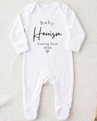 A white onesie with the text "Baby Harrison Coming Soon 2026" printed on it.