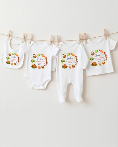 A row of four white baby clothes, including bodysuits and pajamas, hanging on a clothesline.