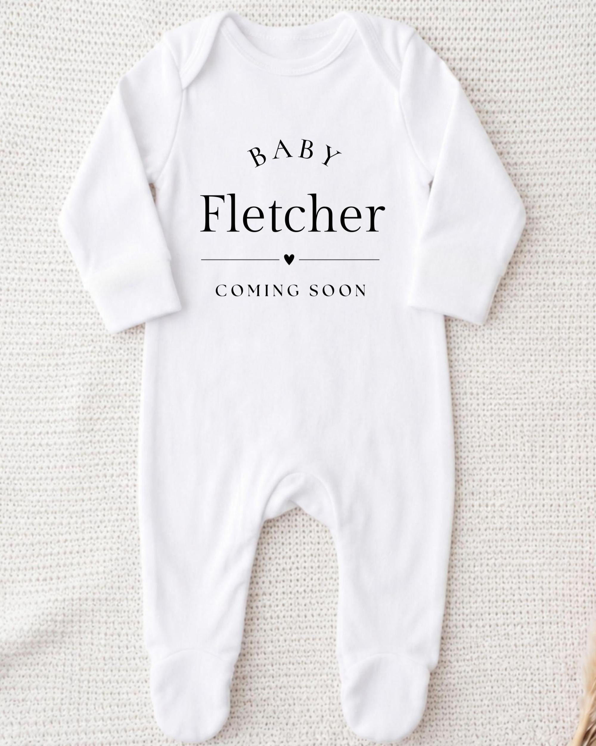 A white onesie with the text "BABY FLETCHER COMING SOON" printed on it.