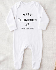 A white onesie with the text "BABY THOMPSON #2 Due Dec 2027" printed on it.