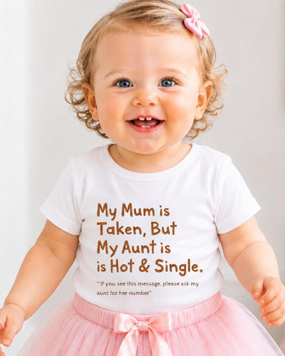 A smiling baby girl wearing a white t-shirt with text and a pink bow in her hair.