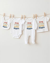 A row of four white baby clothes with the text "Stay Trippy Little Hippie" printed on them, hanging on a clothesline.