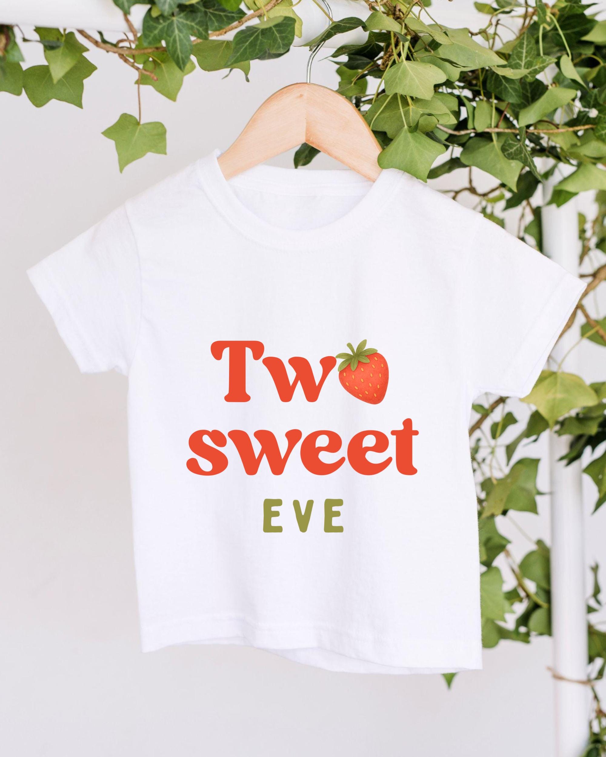 A white t-shirt with the text "Two sweet Eve" printed on it, along with a red strawberry graphic.