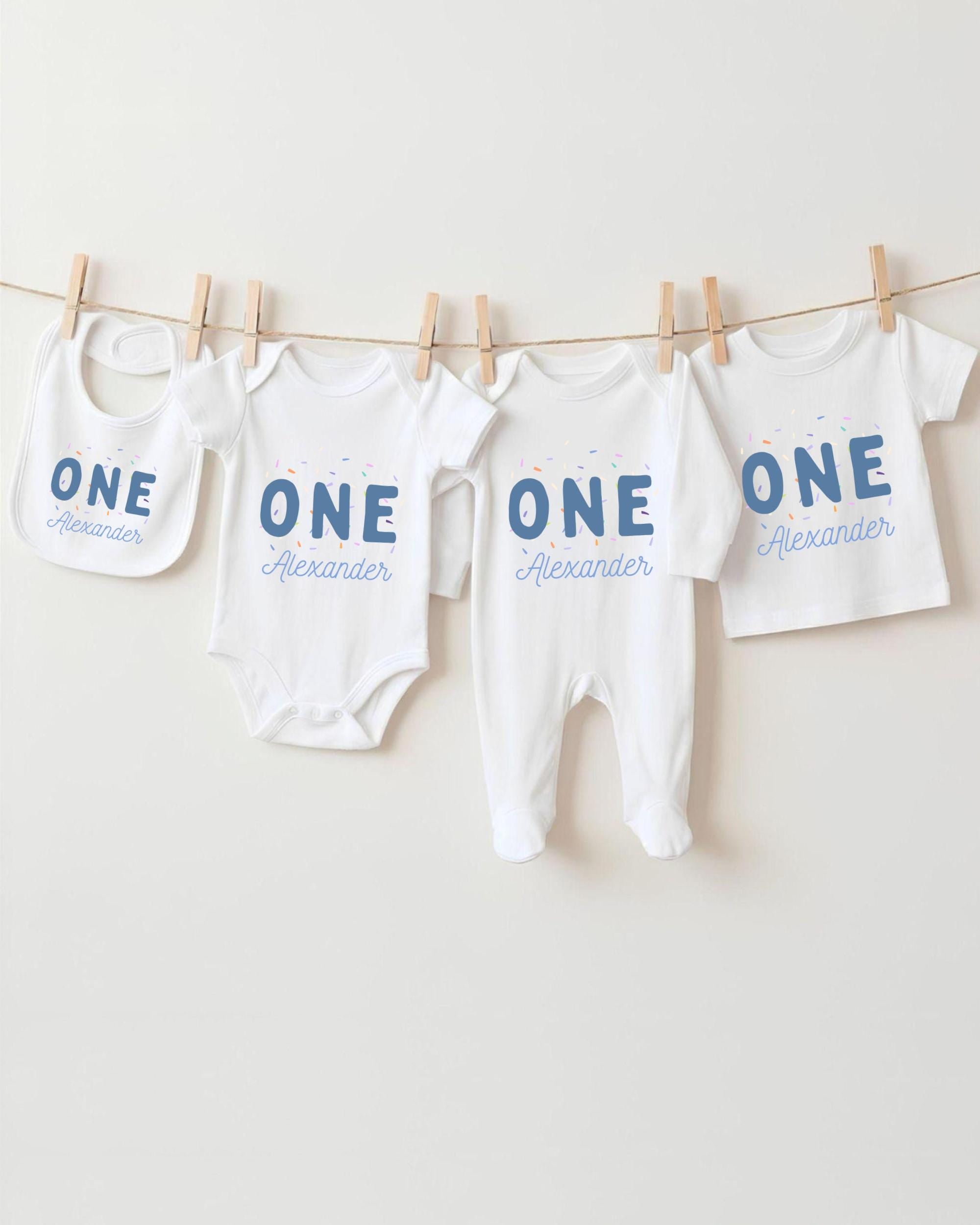 A row of four white baby clothes with the name "Alexander" printed on them, hanging on a clothesline.