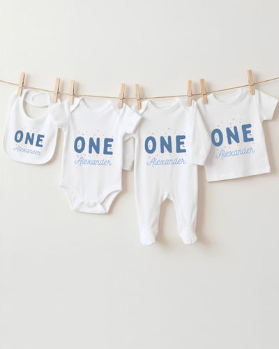 A row of four white baby clothes with the name "Alexander" printed on them, hanging on a clothesline.