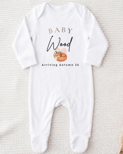 Personalisable white Baby Grow with beige 'BABY', black script 'Wood', a sleeping orange fox and 'Arriving Autumn 26' lettering.